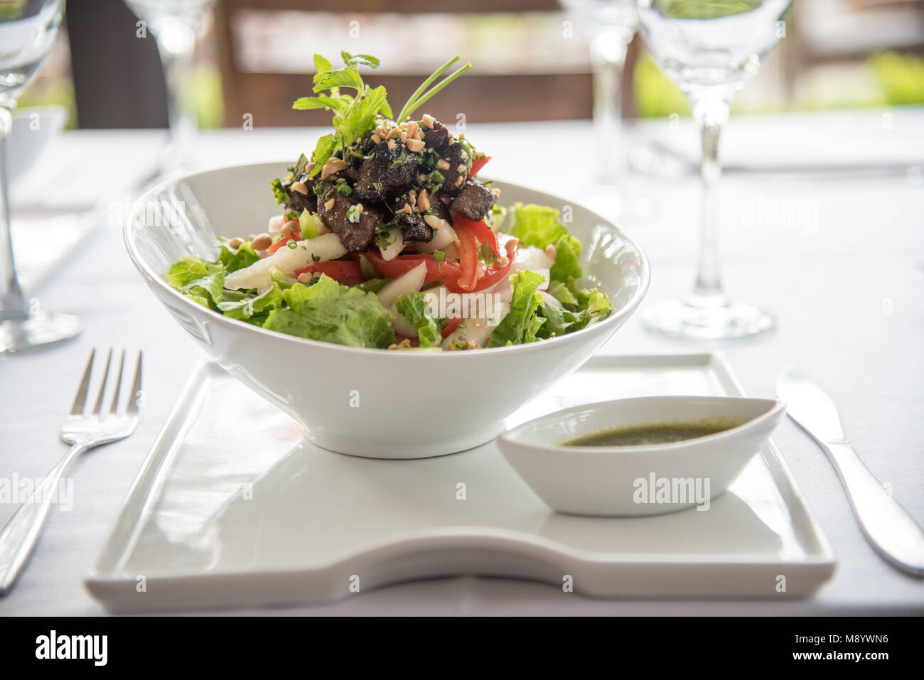 In der Nähe von wunderschönen, grünen Salat in weißem Porzellan Schüssel serviert. Im Restaurant mit weißen Tischdecken und Besteck in Aussicht serviert. Stockfoto