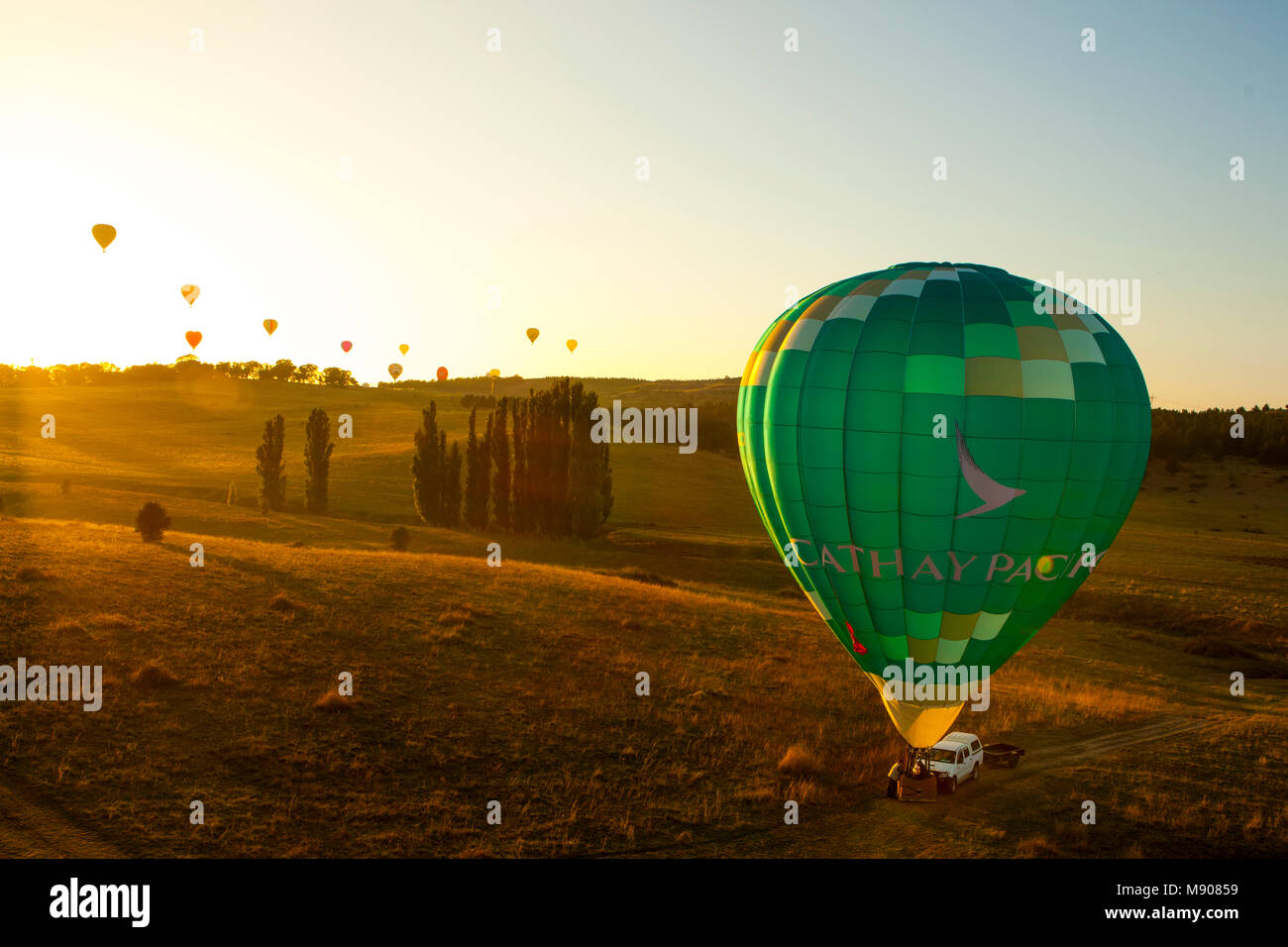 Grüne ballon Bereit zum Abheben, während eine Gruppe von Luftballons bis über den Horizont mit dem Sonnenaufgang steigen. Teilnehmenden Canberra Hot Air Balloon Festival Stockfoto