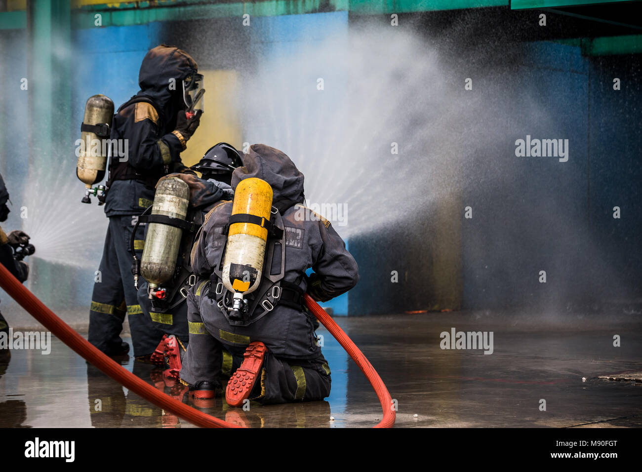 Feuerwehrleute mit Wasser aus einem Schlauch zur Brandbekämpfung bei feuergefecht Ausbildung der Versicherungsgruppe. Feuerwehrmann tragen ein Feuer Anzug für Sicherheit unter die Gefahr Stockfoto