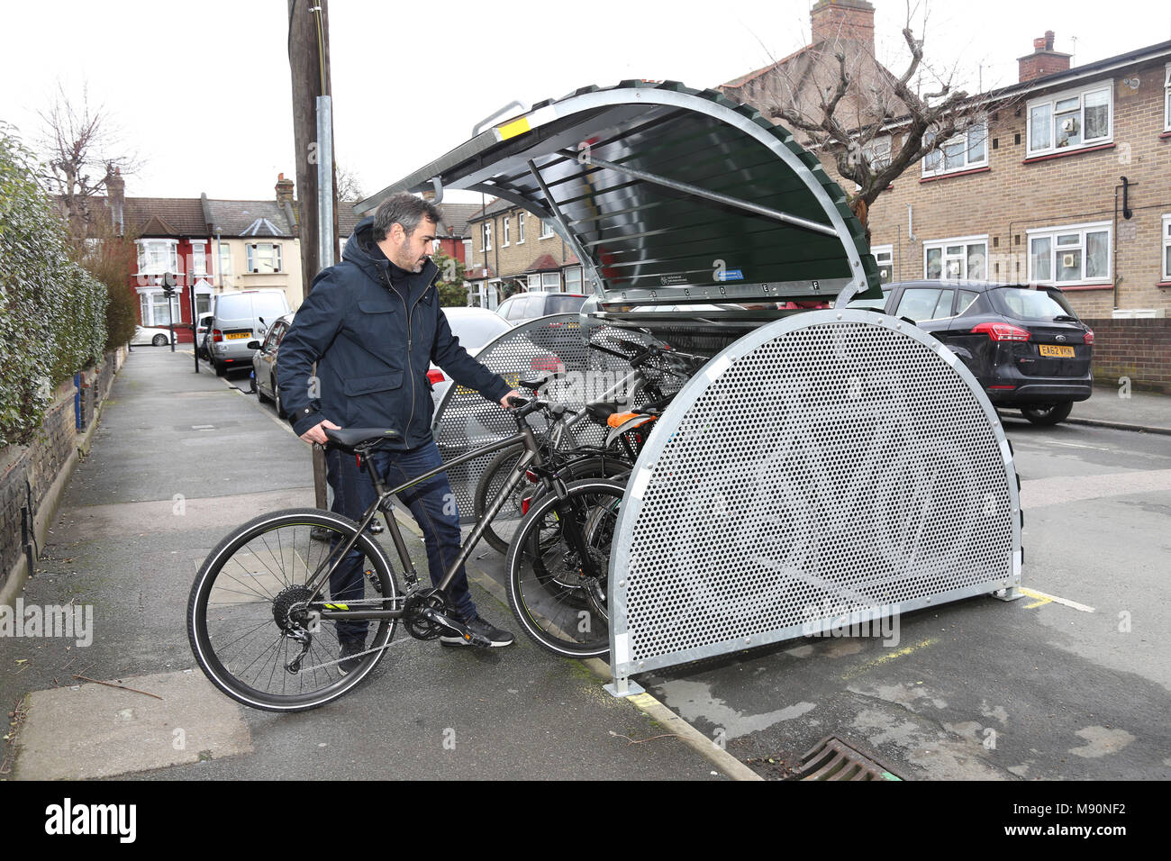 Ein Radfahrer Orte sein Fahrrad in eine sichere auf der Straße Fahrrad geschäft kürzlich auf einer ruhigen Londoner Straße installiert. Stockfoto