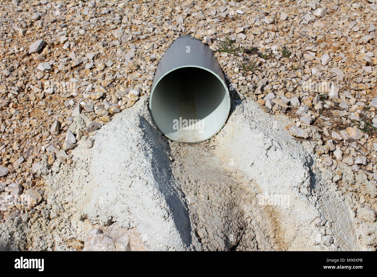 Kunststoff Wasserleitung Entleeren mit Kies kleine getrocknete Gras umgeben und Beton auf sonnigen Wintertag Stockfoto
