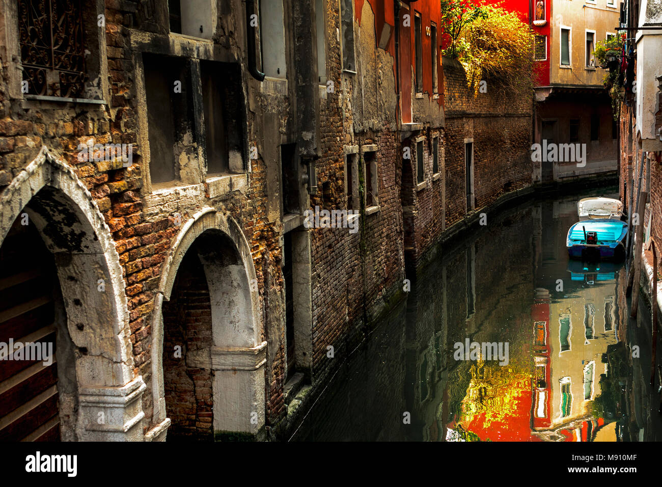 Schmalen schattigen Kanal Route der alten zerfallenden Mauern Auswuchs der sonnenbeschienenen Laub im Wasser spiegelt und weiß gestrichenen Torbögen und Simsen in Venedig Stockfoto