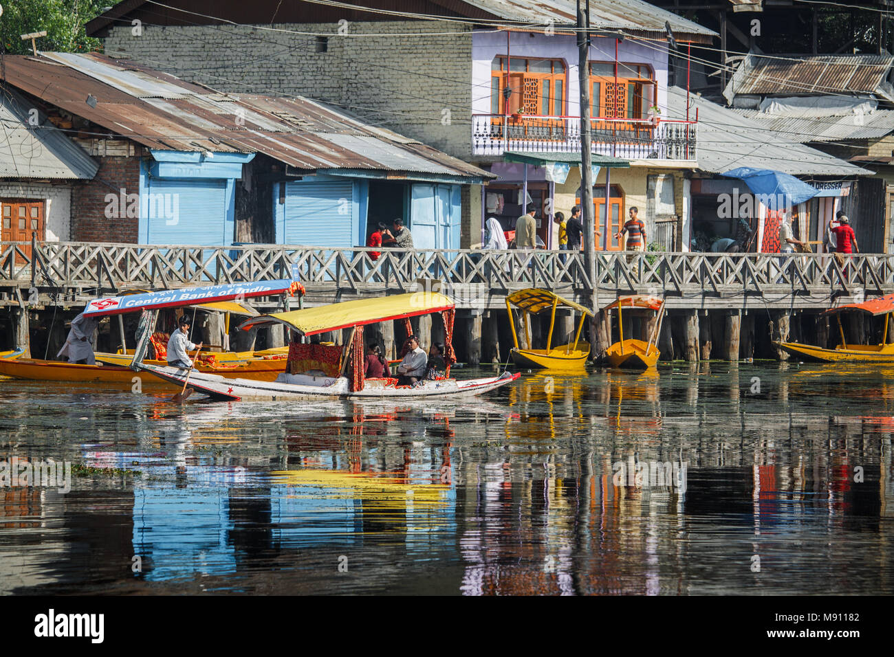 Shikara Sportboote auf Dal Lake in Srinagar, Kashmir. Eine lebendige Reportage Szene mit lakeside Häuser, Holz- Promenade und Wasser Reflexion Stockfoto