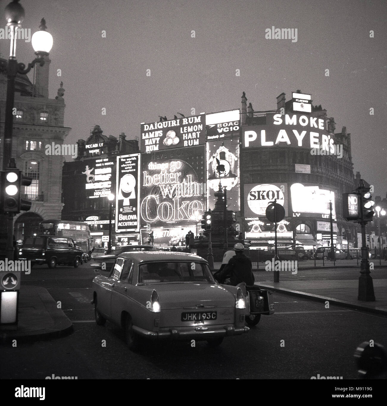 1960, historische Bild von London Piccadilly Circus am Abend mit Fahrzeugen und dem berühmten Neonröhren und Werbetafeln für Marken wie "Spieler Zigaretten' und 'Coca-cola'. Stockfoto