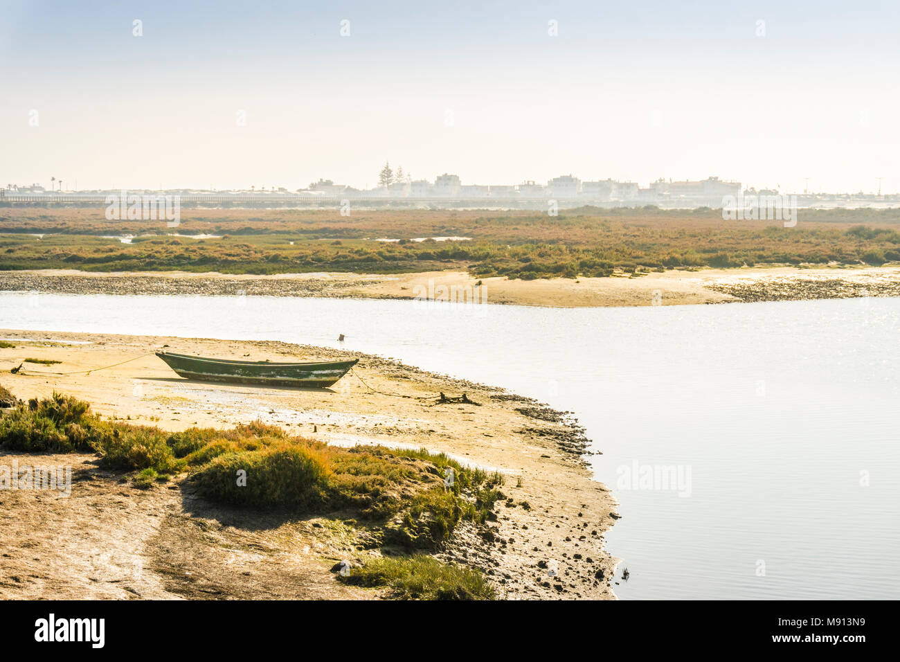Grüne Boot bei Ebbe in der Ria Formosa mit Gebäuden von Faro Beach als Hintergrund, Portugal Stockfoto