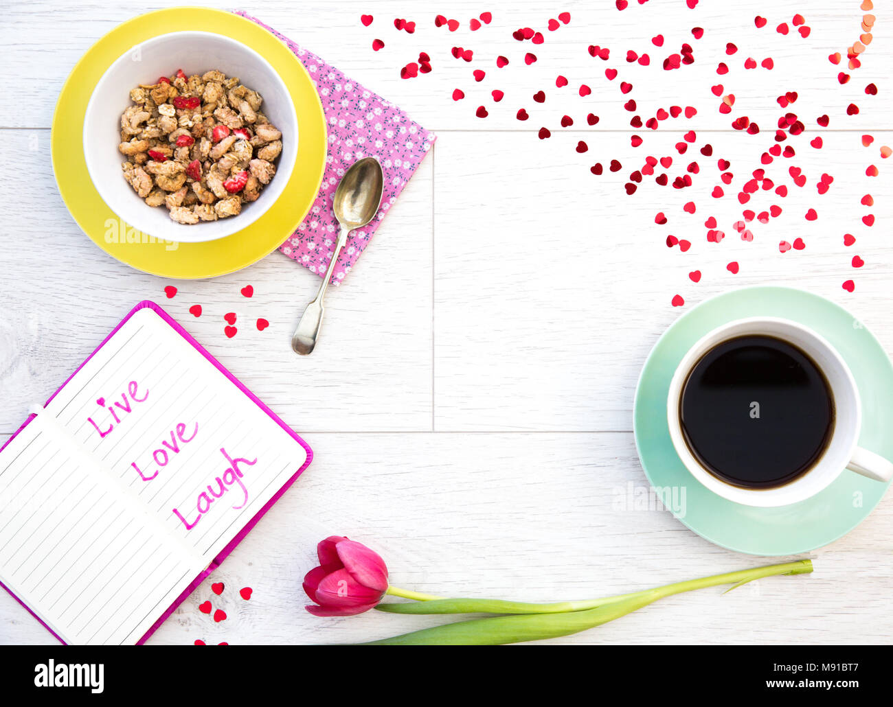 Blick von oben auf ein weißes, Holz- Tisch mit einem weiblichen Frühstück mit Müsli und Kaffee zusammen mit Tulpen, Blumen und einem Notebook gefüllt Stockfoto