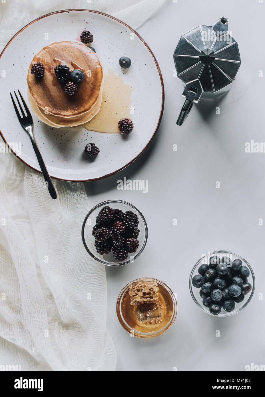 Draufsicht auf das leckere Frühstück mit Pfannkuchen, Beeren, Honig und Kaffee auf Grau Stockfoto