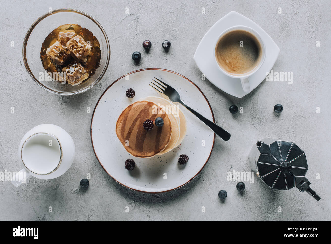 Blick von oben auf die süß lecker Pfannkuchen mit Kaffee, Milch, frische Beeren und Honig auf Grau Stockfoto