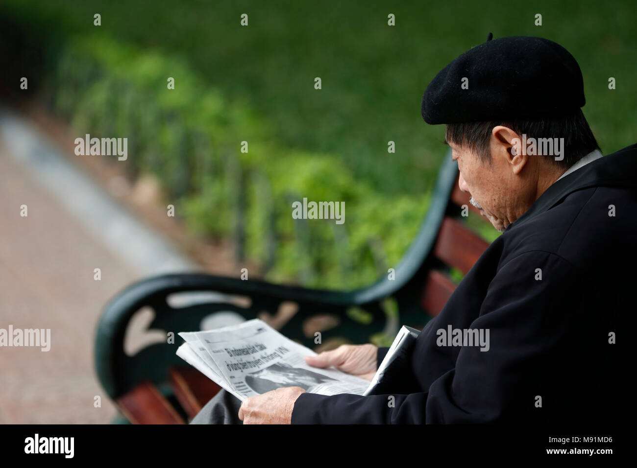 Alten vietnamesischen Mann sitzt auf der Bank mit Zeitung. Hanoi. Vietnam. Stockfoto