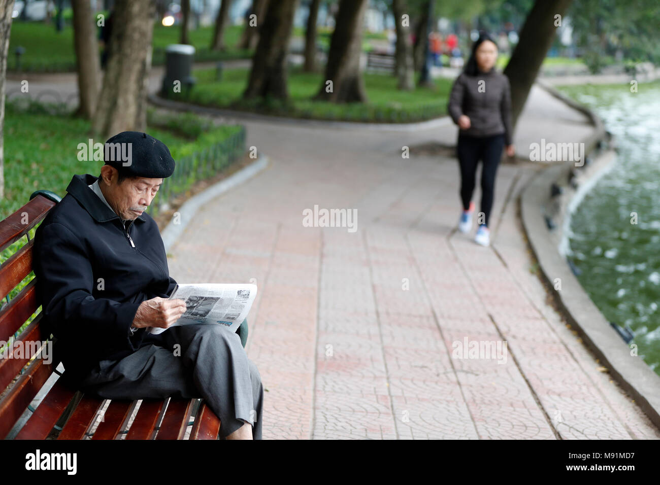 Alten vietnamesischen Mann sitzt auf der Bank mit Zeitung. Hanoi. Vietnam. Stockfoto