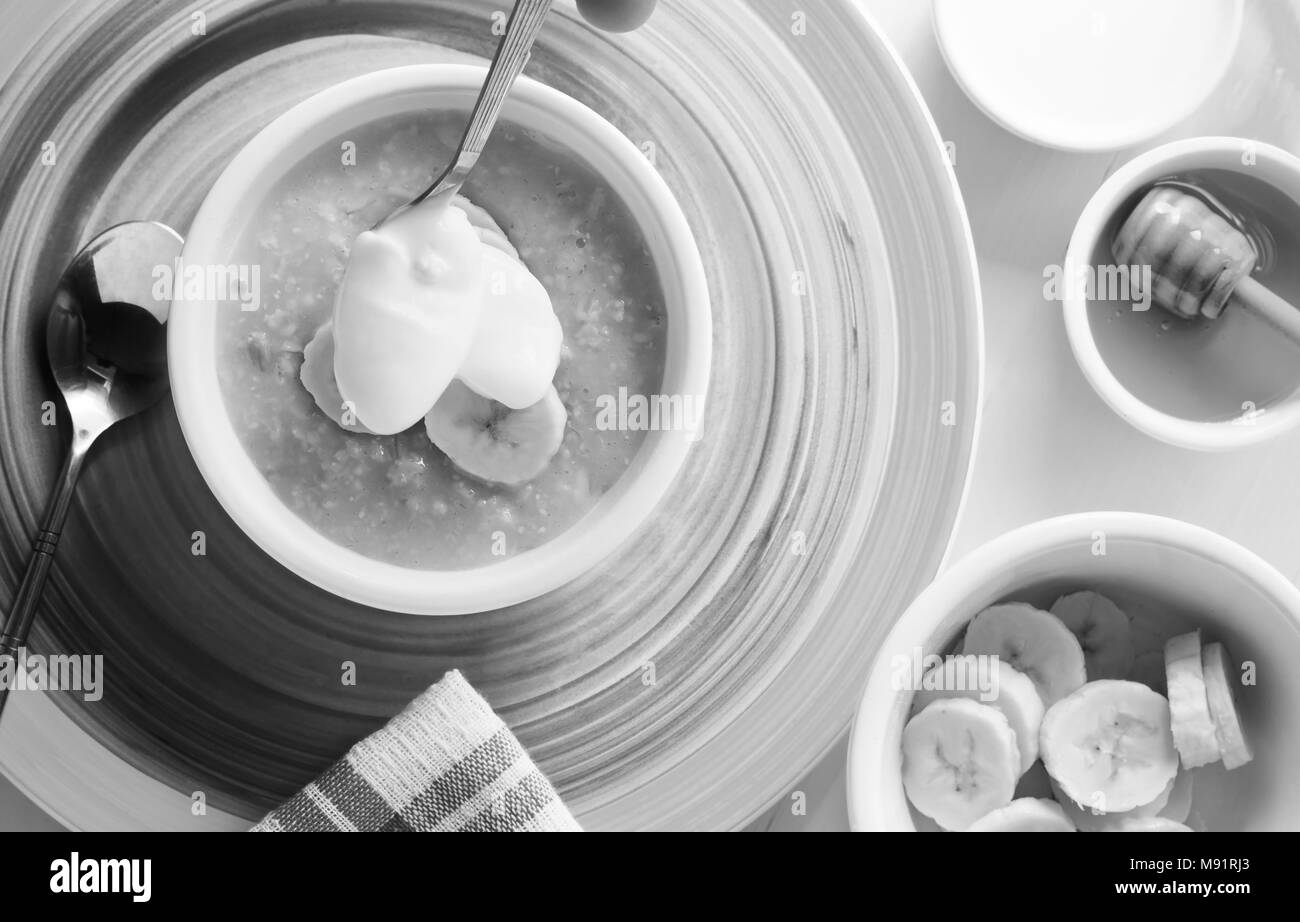 Ein Frühstückstisch von organischen heissen Brei und Banane mit Honig. Schwarz und Weiß Stockfoto