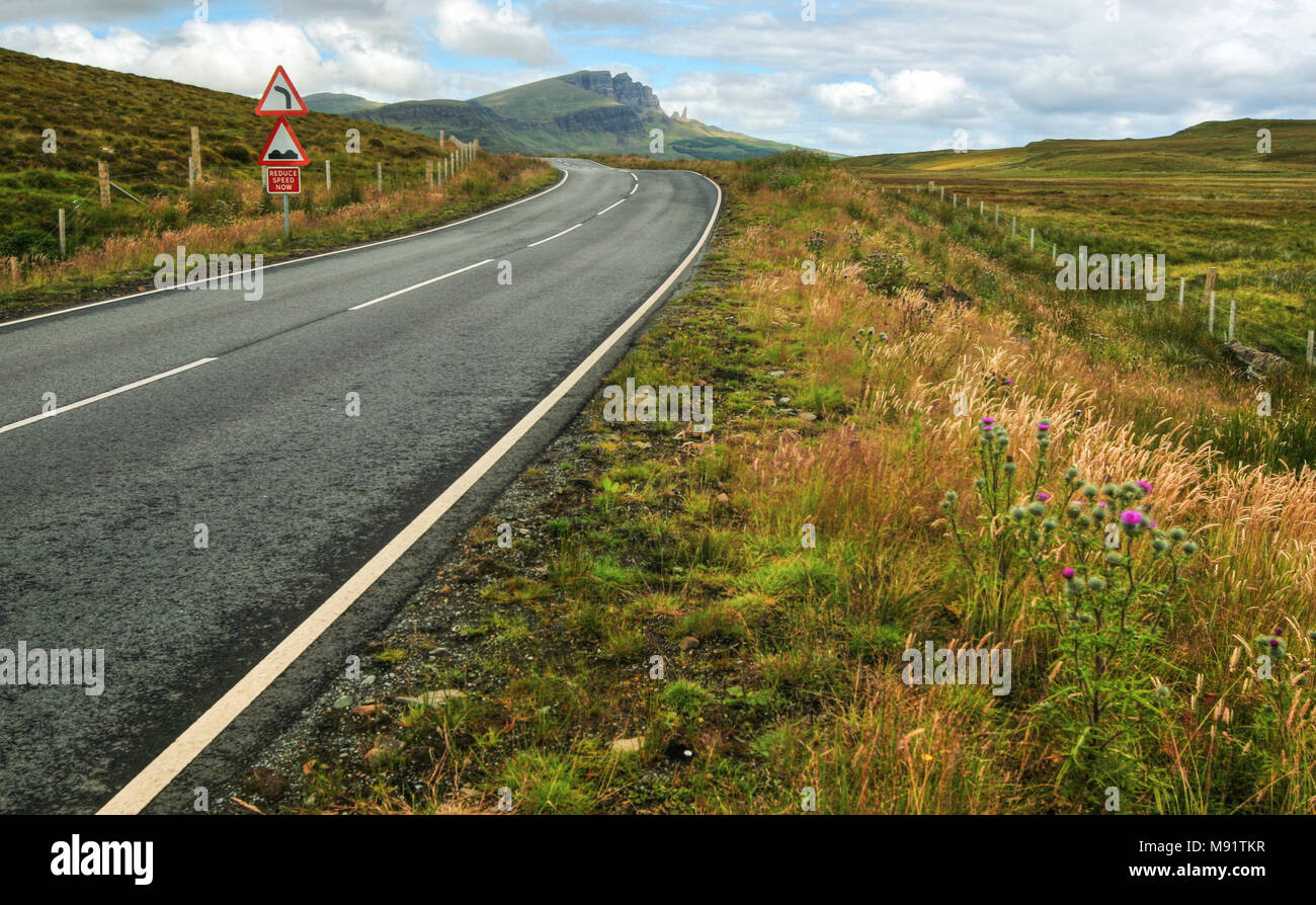Weite Einstellung auf leere Straße, Kurve, Stößen und Geschwindigkeit reduzieren Jetzt anmelden mit alten Mann von Storr Berg im Hintergrund. Isle of Skye, Scotland, United Kingd Stockfoto