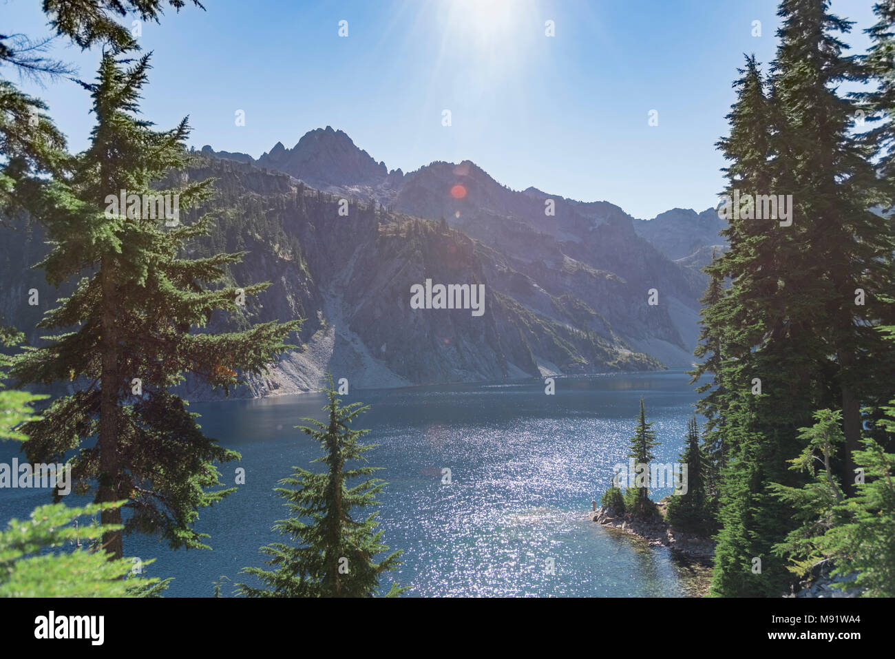 Unberührten alpinen See im Sommer von immergrünen Pinienwald späten Tag Sonnenstrahlen umgeben. Stockfoto