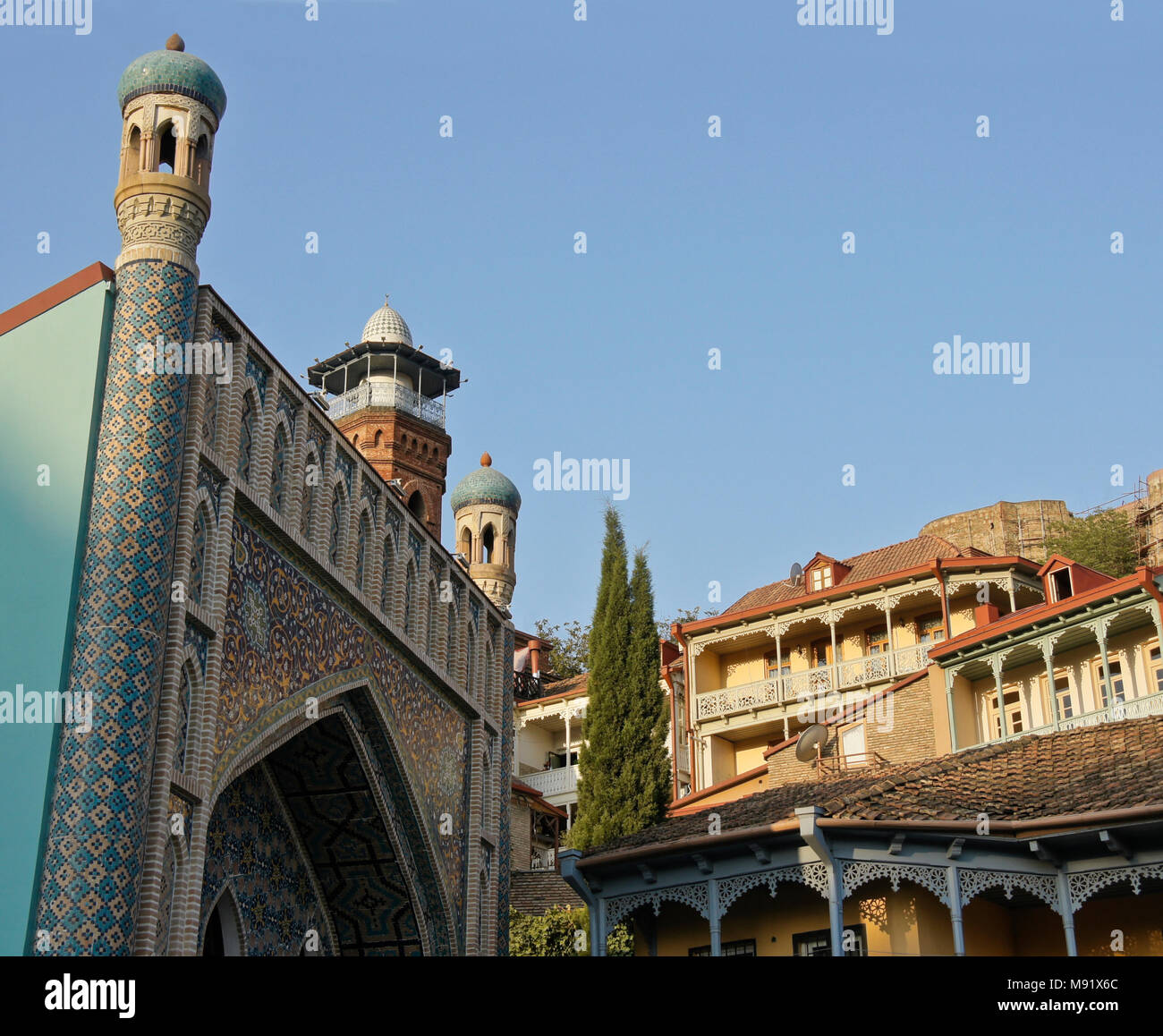 Die blau gekachelte Fassade des Orbeliani Bäder, aus rotem Backstein, Minarett einer Moschee, mit Balkonen, Häuser in der Altstadt und die Festung Narikala auf Hügel, Tiflis, Georgien Stockfoto