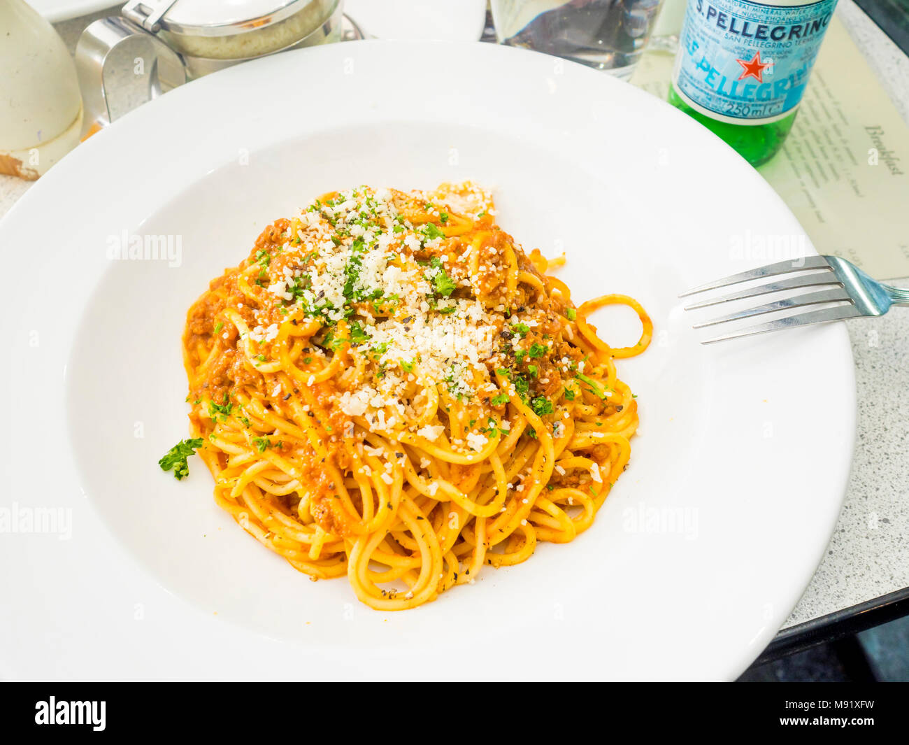 Italienisches Restaurant Hauptgericht Spaghetti Bolognese mit Parmesan, schwarzer Pfeffer und S. Pellegrino Mineralwasser Stockfoto