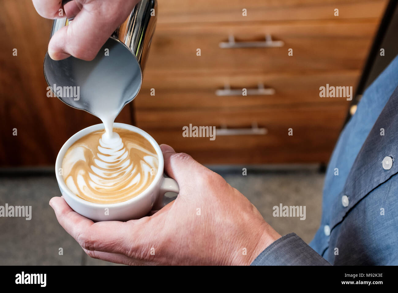 Professionelle barista Gießen gedämpfte Milch aus Edelstahl Becher in die Tasse Kaffee, latte Art auf Cappuccino Stockfoto