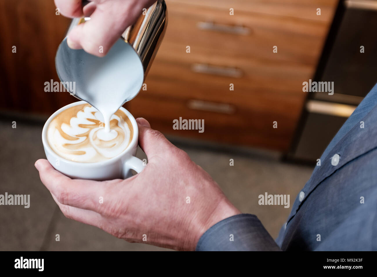 Professionelle barista Gießen gedämpfte Milch aus Edelstahl Becher in die Tasse Kaffee, latte Art auf Cappuccino Stockfoto