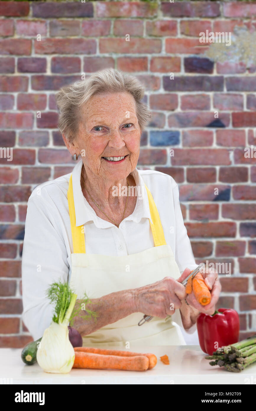Ältere Frau mit grauen Haaren kochen in Alten roten Ziegelmauer Küche - Gemüse Stockfoto