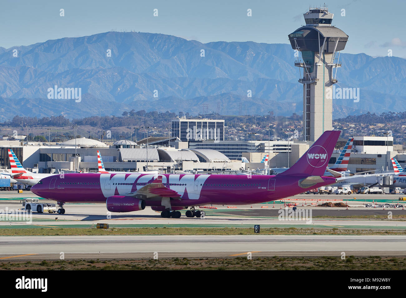 WOW Air Airbus A330-300 Abschleppen zu den Tom Bradley Terminals am Internationalen Flughafen von Los Angeles, LAX, der Tower und die Berge dahinter. Stockfoto