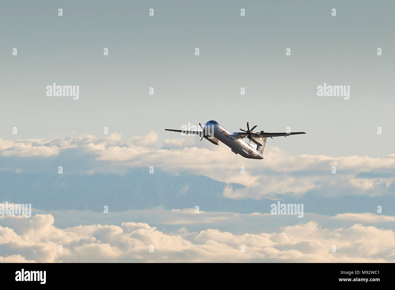 Horizon Air Bombardier Dash-8-Q400 In Alaska Airlines Livree, Klettern aus Los Angeles. Wolken über die Stadt und die schneebedeckten San Gabriel Mountains Stockfoto