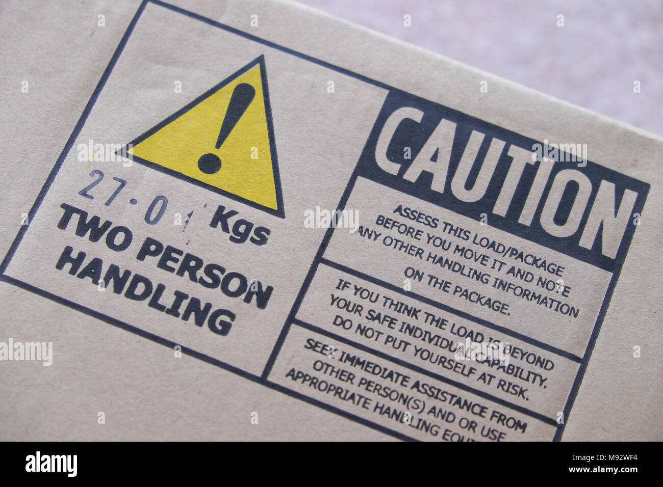 Vorsicht schwere Last zwei Person Umgang mit Warnschild am 27 kg Box Stockfoto