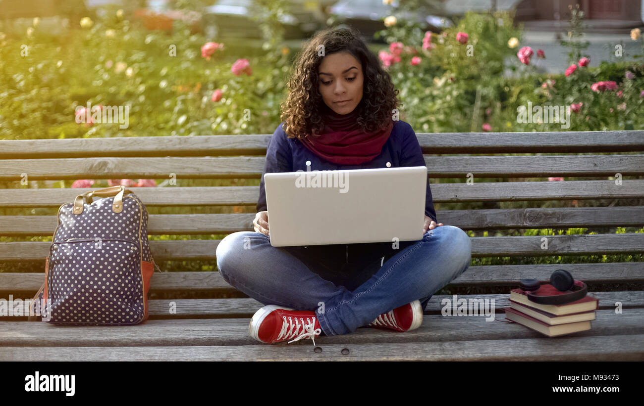 Ernsthafte Schülerin mit Freunden zu reden über Laptop Kamera, sitzt auf der Bank Stockfoto