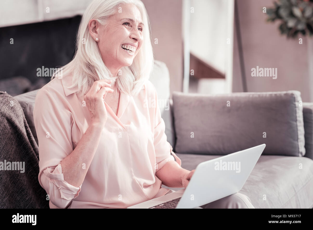 Freudige angenehme Frau sitzt auf dem Sofa und lächelt. Stockfoto