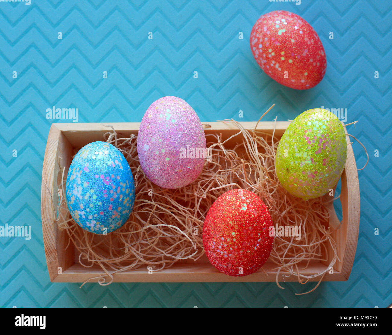 Fünf bunte Ostereier in eine Holzkiste mit Nistmaterial im Inneren auf einem Pastell-blaue Hintergrund Stockfoto