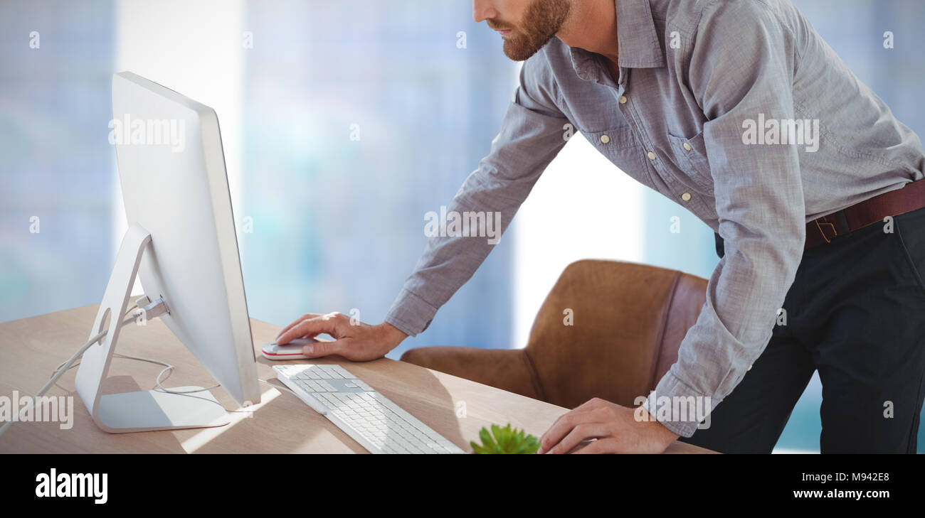 Das zusammengesetzte Bild der Geschäftsmann mit Computer, während am Schreibtisch stehend Stockfoto