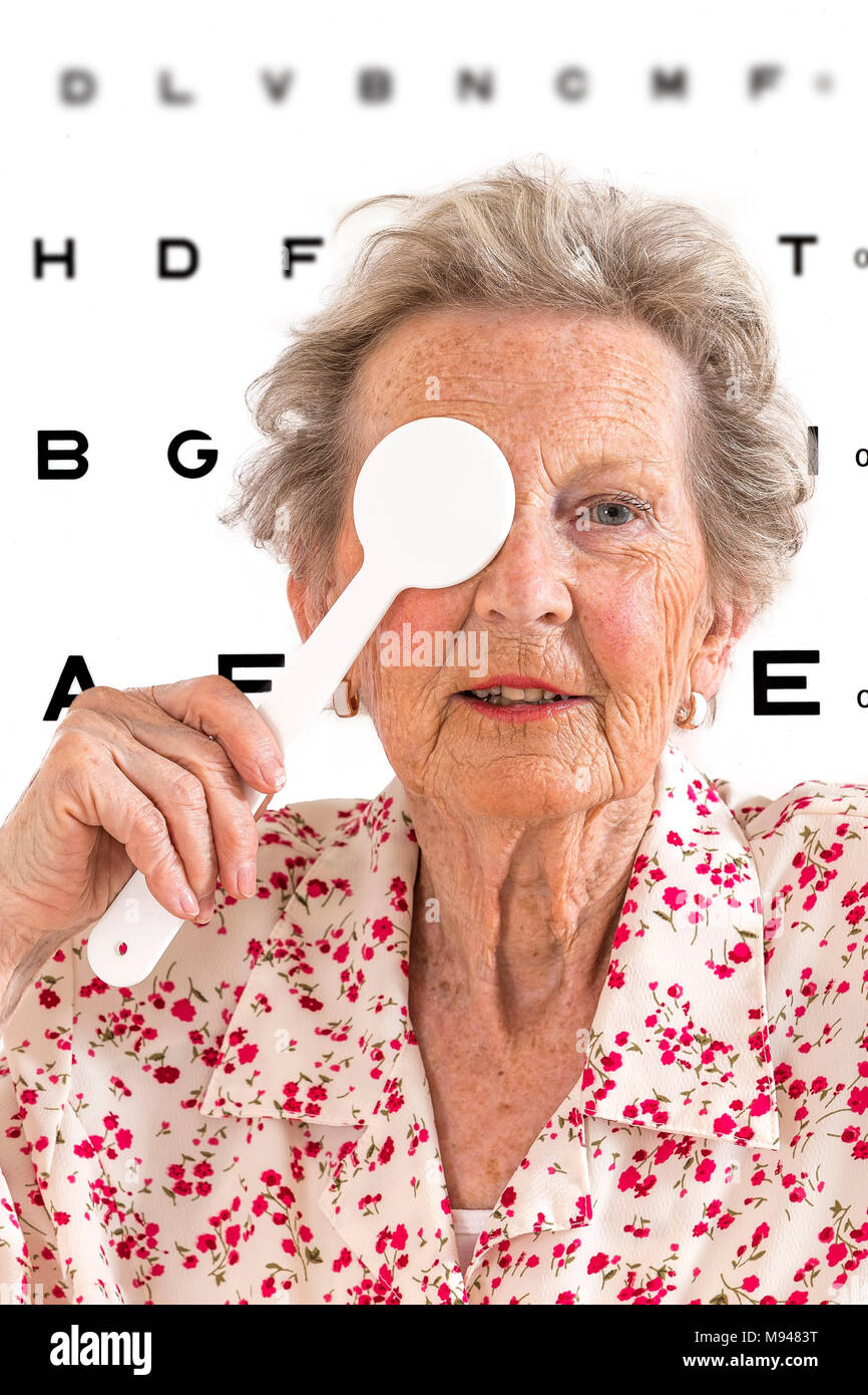 Ältere Dame, eine Sehkraft test Untersuchung bei einem Optiker Klinik whith Auge Diagramm Abbildungen auf Hintergrund Stockfoto