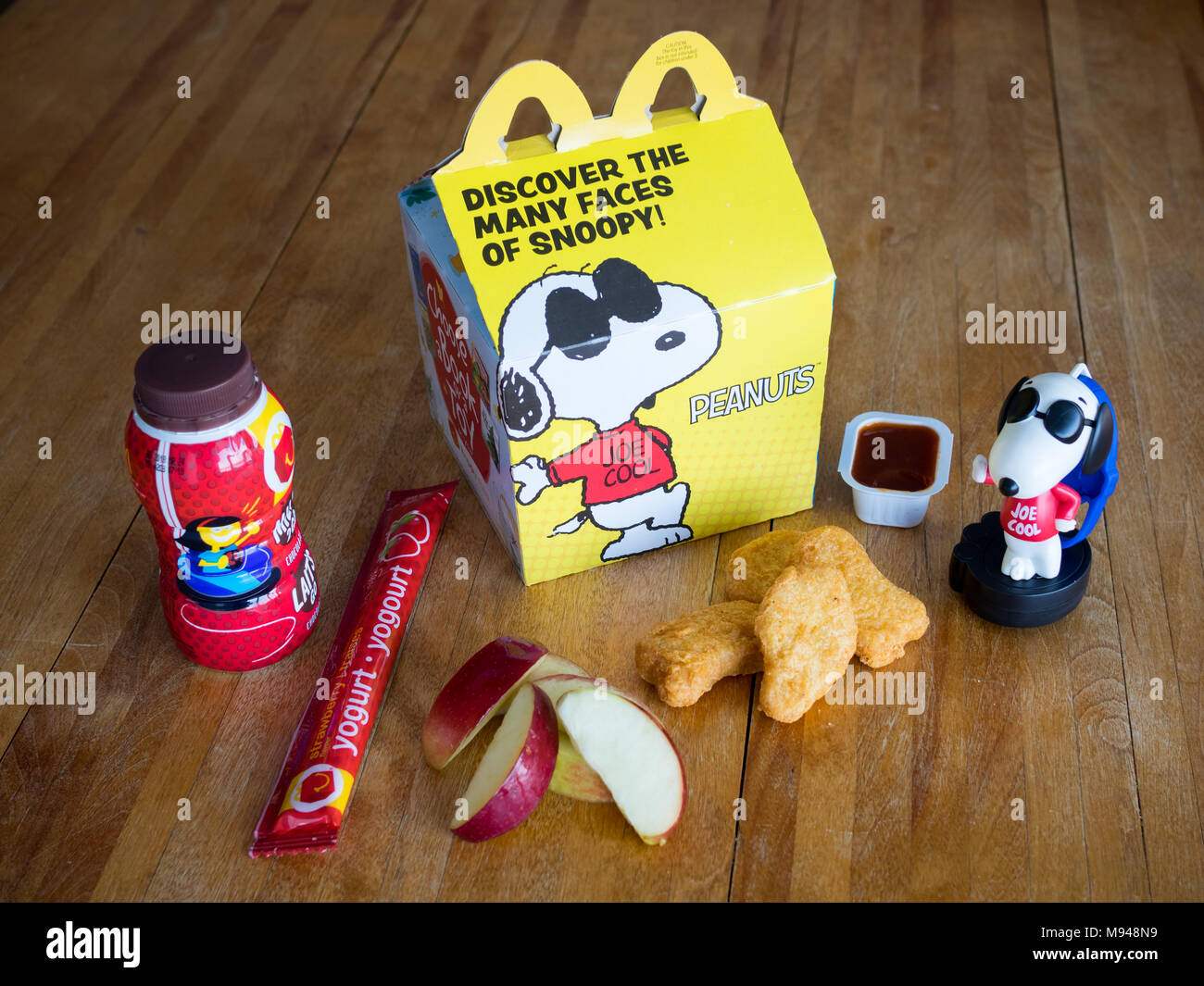 Ein McDonald's Happy Meal mit Chicken McNuggets, Apple Keile, Schokolade, Milch, Joghurt, und Snoopy Spielzeug. Stockfoto