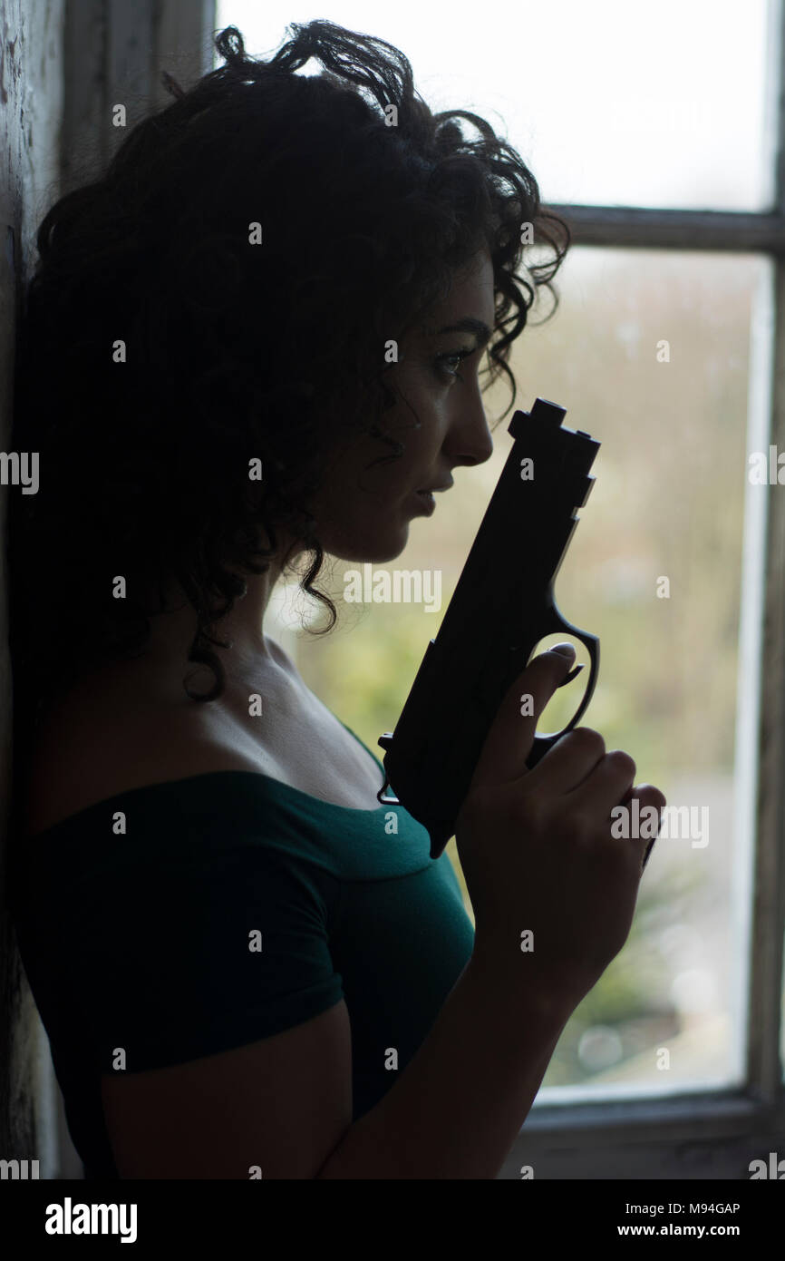 Junge Frau mit einer Pistole am Fenster Stockfoto