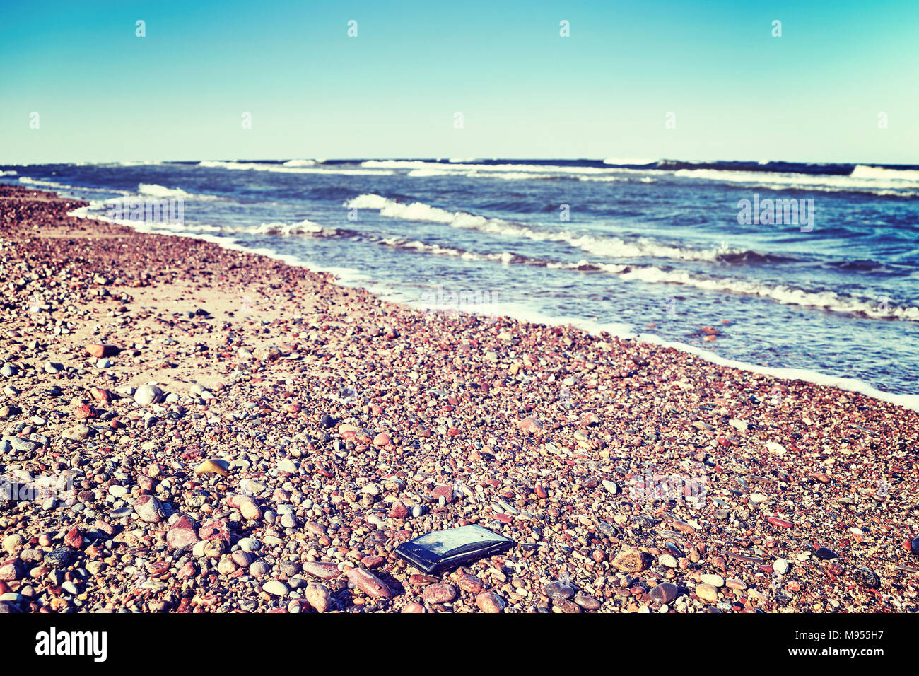 Gebrochene Handy mit gebrochenen Bildschirm auf einem steinigen Strand, selektiver Fokus, Farbe getonte Bild. Stockfoto