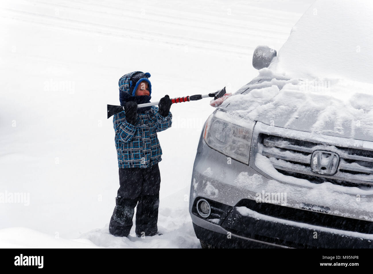 Ein Junge (5 Jahre alt) Bürsten frisch gefallenen Schnee von einem Auto in Quebec, Kanada Stockfoto