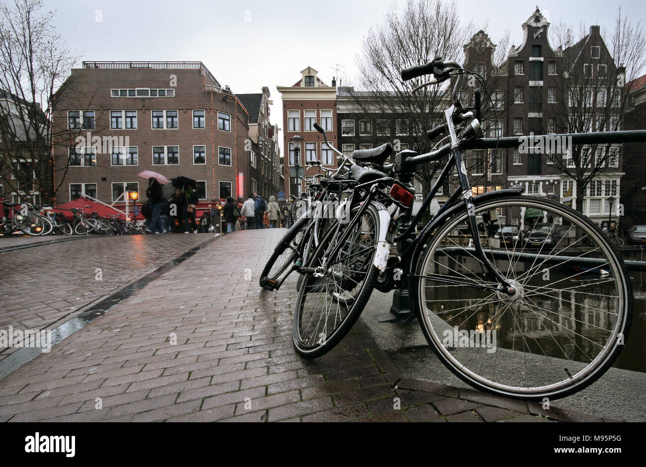 Amsterdam, Niederlande, 23. März 2008: schwarz Fahrräder nass vom Regen auf der Brücke geparkt über einen der vielen Kanäle mit Häusern in den Rücken. Stockfoto