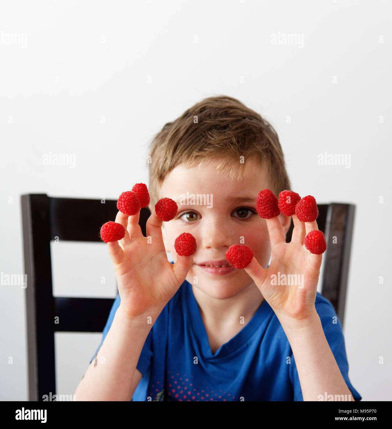 Ein kleiner Junge (5 Jahre alt) mit Himbeeren auf seine Finger Stockfoto