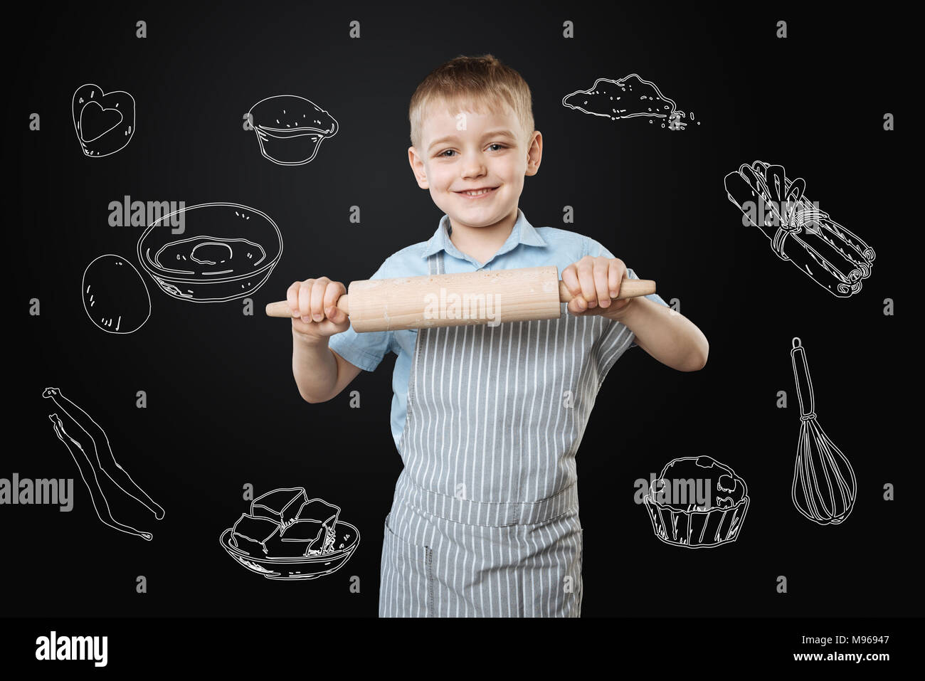 Optimistische Junge mit einem Nudelholz beim Kochen Kuchen für seine Mutter Stockfoto