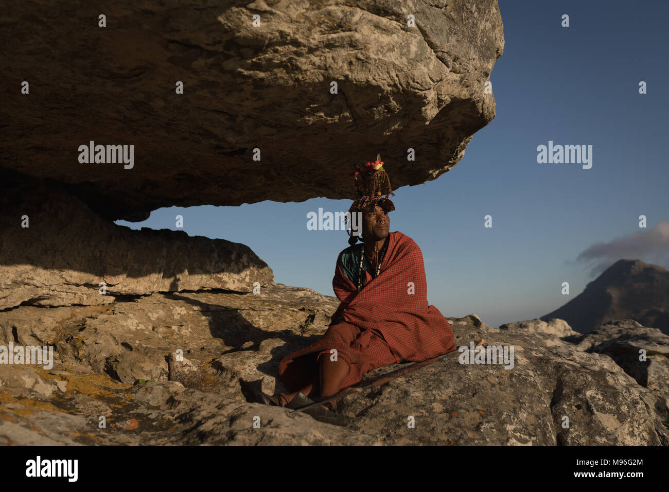 Masai Mann in traditioneller Kleidung sitzt auf Felsen Stockfoto