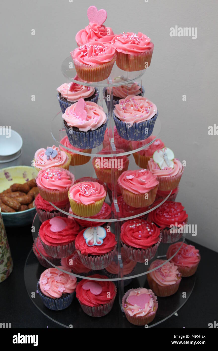 Fünf tier Kuchen stand mit Cupcakes in verschiedenen Schattierungen von rosa Zuckerglasur und Herz Verzierungen bedeckt nur eine Tabelle mit Schüssel von chipolata Würstchen Stockfoto
