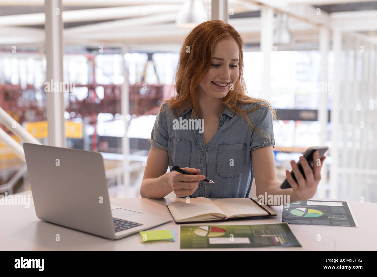 Weibliche Führungskraft mit Handy am Schreibtisch Stockfoto