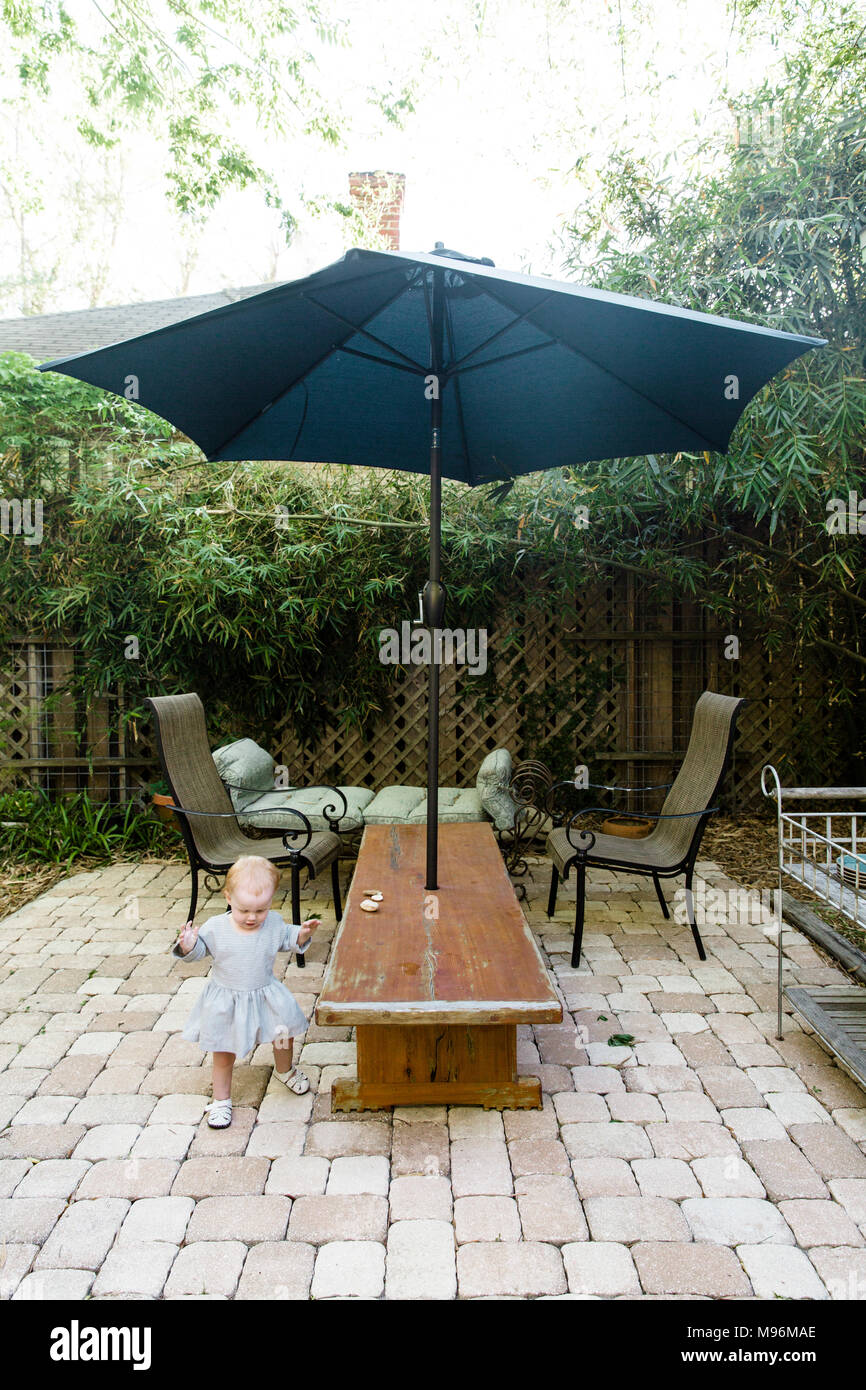Baby zu Fuß außerhalb Garten mit Stühlen und Sonnenschirm Stockfoto