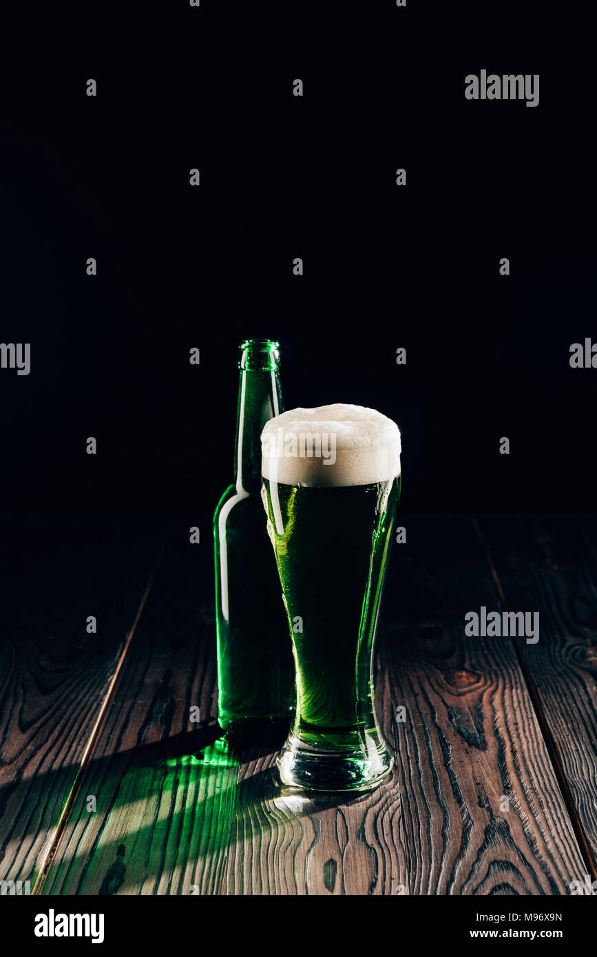 Leuchtendes Glas und Flasche grün Bier auf Holztisch, st patricks day Konzept Stockfoto