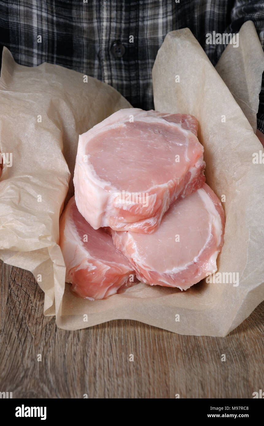 Ein Haufen von frischen gehackten rohes Schweinefleisch Steaks über die Knochen in Geschenkpapier in den Händen eines Mannes Stockfoto