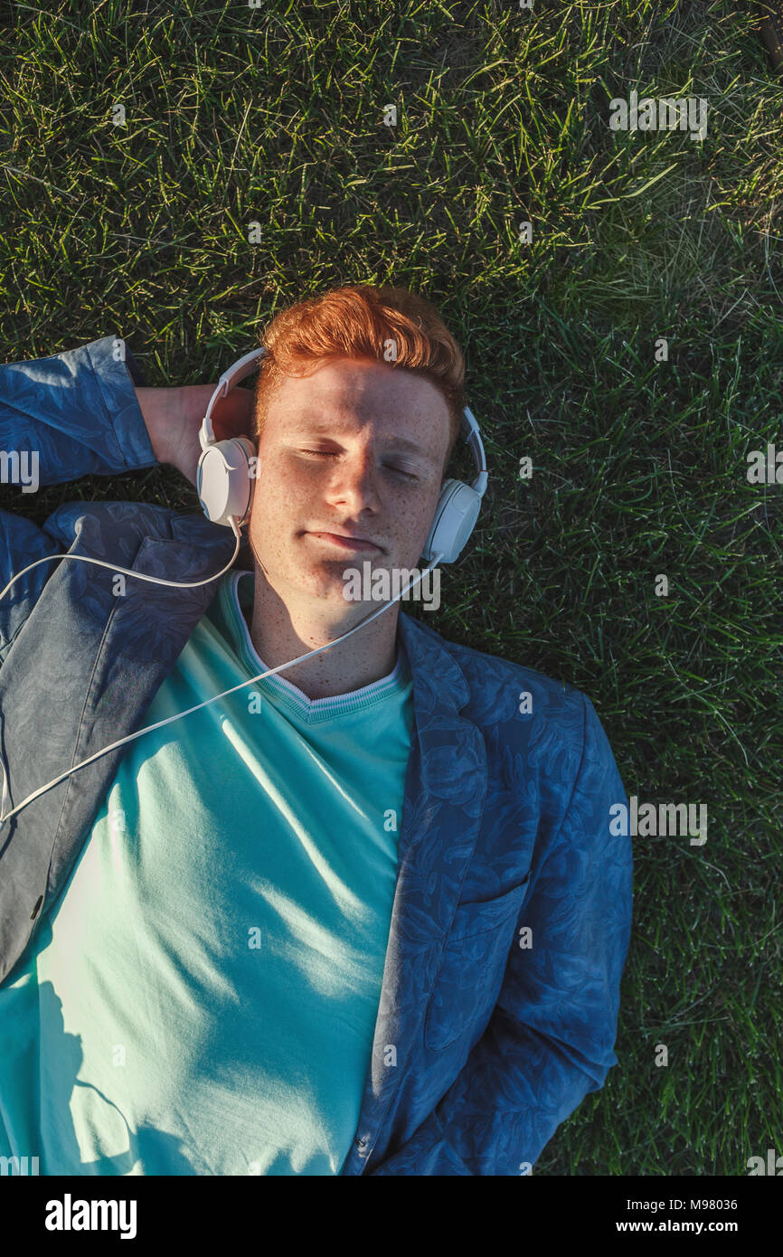Rothaarigen jungen Mann mit Kopfhörer liegen auf Gras Stockfoto