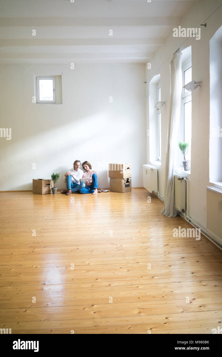 Reifes Paar sitzt auf dem Boden in den leeren Raum neben Kartons mit Tablet Stockfoto
