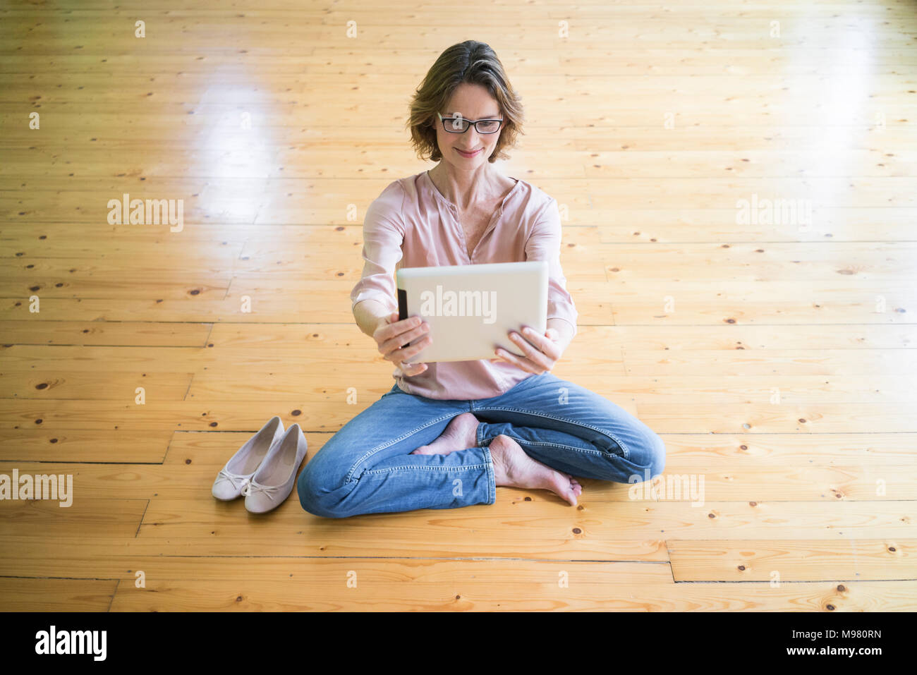 Lächelnd reife Frau sitzt auf der Holzboden unter selfie mit Tablet Stockfoto