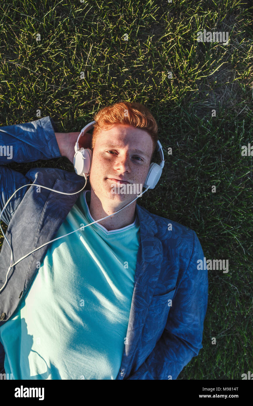 Portrait von rothaarigen Jungen Mann mit Kopfhörer liegen auf Gras Stockfoto