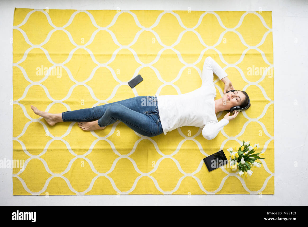 Lächelnde Frau mit Kopfhörern liegen auf Teppich mit Bündel Tulpen Stockfoto