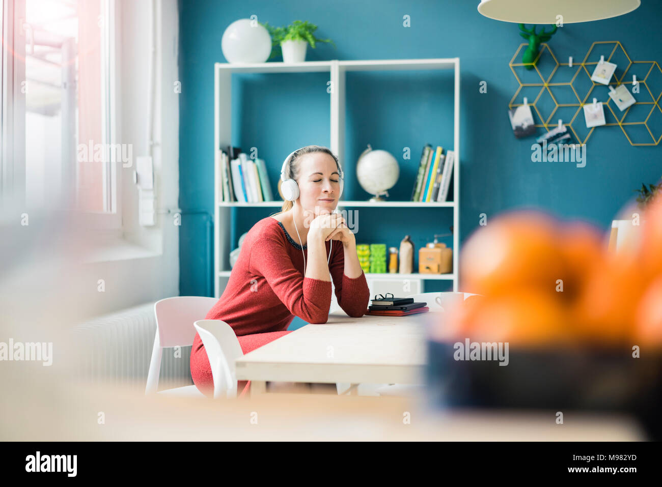 Frau mit geschlossenen Augen sitzen am Tisch lisening Musik über Kopfhörer Stockfoto