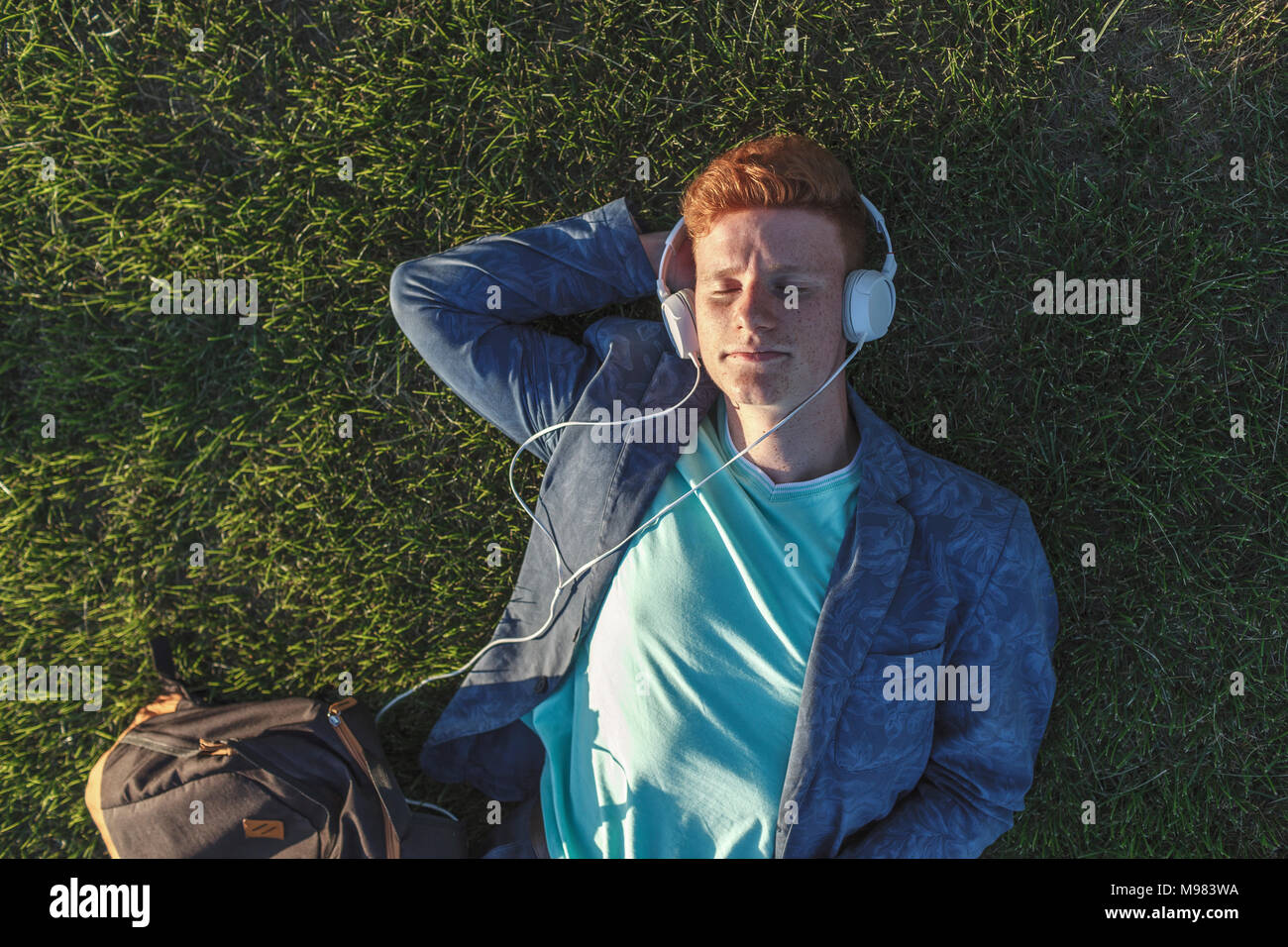 Rothaarigen jungen Mann mit Kopfhörer liegen auf Gras Stockfoto